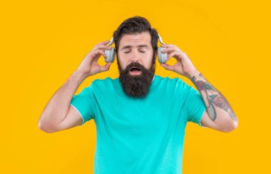 Şok olmuş adam kulaklıkla yüksek sesle müzik dinliyor. Yüksek sesli kulaklıklı rahatsız bir adam. Yüksek sesli müzikle rahatsız bir adamın stüdyo çekimi. Sinirli adamın sarı kulaklıklarda yüksek sesli müziği var..