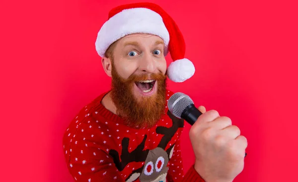 christmas music party. surprised man at christmas music party with microphone. christmas santa man at music party isolated on red background.