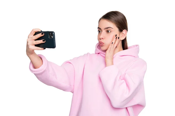 stock image Young woman in pink hoodie pouting lips holding smartphone in hand isolated on white, selfie.