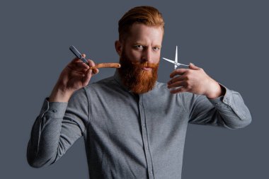 Gri arka planda izole edilmiş insan berberinin portresi. Berber dükkanında elinde makas olan bir adam. Berber dükkanındaki berber. Berber adam kuaförde makas ve bıçak tutuyor. Berber dükkanı konsepti.