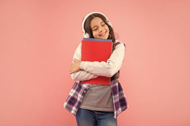 Çalışma kitabı olan neşeli genç kız pembe arka planda kulaklık takıyor, bilgi sahibi..