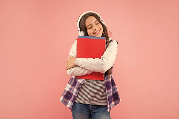 戴着粉红背景 知识的耳机 拿着工作手册的快乐的少女 — 图库照片