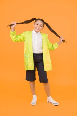 Su geçirmez konsept. Sevimli çocuk. Mutlu liseli kız sarı arka planda yağmurluk giyiyor. Küçük liseli kızlar yağmurlu günlerde suya dayanıklı kıyafetler giyerler. Tatlı liseli kız kendini bahar havası için korunmuş hissediyor..