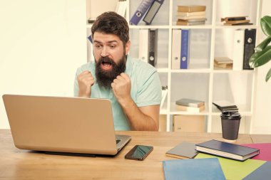 Heyecanlı iş adamı ofis masasında dizüstü bilgisayara bakıp yumruk atıyor..