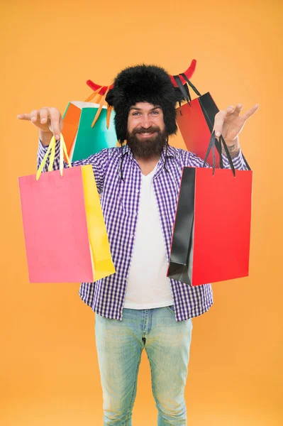 stock image Keep smiling and carry on bags. Bearded man smiling with paper bags after seasonal sale. Happy hipster in bull horns hat holding shopping bags. Carrying purchases in colorful non grocery carrier bags.