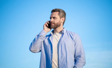 Telefonda konuşan bir adamın iletişimi. Adam akıllı telefondan konuşuyor. Gökyüzü arka planında insan iletişimi.