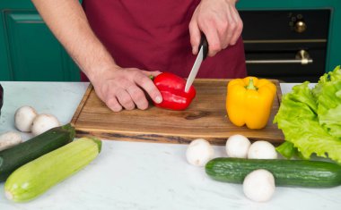 Eller kırmızı biber ahşap kesme tahtası üzerinde bıçakla kesti. Sebze, salata, salatalık, kabak, mantar, vitamini. Vejetaryen, sağlık, diyet kavramı. Yemek pişirme, hazırlık,.
