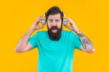 Şaşırmış adamın sarı kulaklıklı yüksek sesli müziği var. Sinirli adam kulaklıkla yüksek sesle müzik dinler. Yüksek sesli kulaklıklı rahatsız bir adam. Yüksek sesli müzikle rahatsız bir adamın stüdyo çekimi..