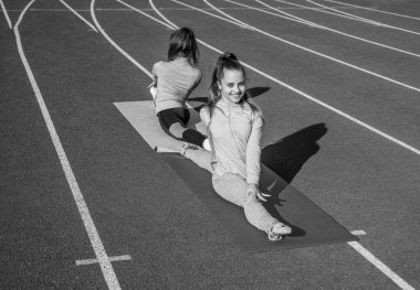 Happy fit girls do splits on stretch mat on athletics track, pilates.