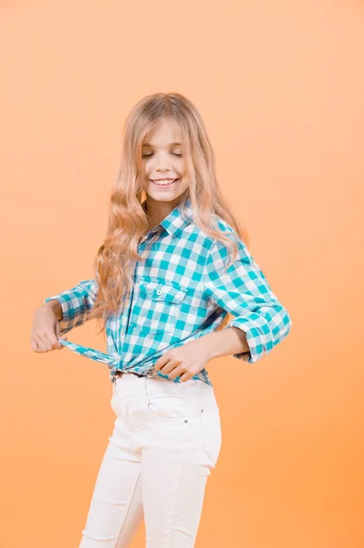 青い格子縞のシャツとオレンジ色の背景に白のパンツで笑顔長い髪閉じた目 金髪の女の子モデル 子供ファッション スタイル トレンド コンセプト 美しさ — ストック写真