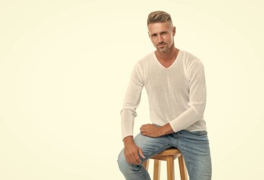 Gülümseyen, gri saçlı, olgun, beyaz arka planda izole bir şekilde oturan, erkeklerin güzelliği..