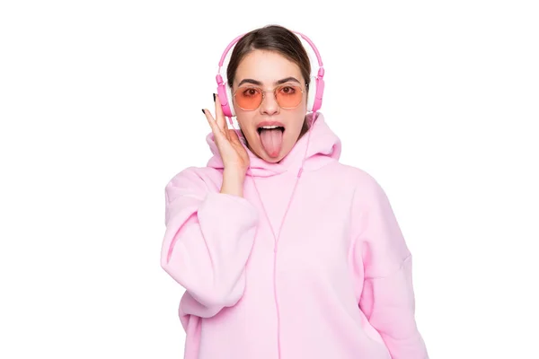 女の子でピンクパーカーと眼鏡で音楽を聴くでヘッドフォンステッキング舌アウト島の上に白 — ストック写真