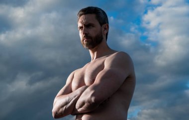 Üstsüz, kaslı adam. Kaslı gövdeli maço bir adam. Gökyüzündeki atletik adam.