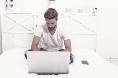 Handsome guy in pajamas use laptop computer modern technology for working from home during coronavirus COVID-19 pandemic lockdown, telework.