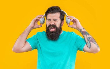 Sinirli adam bağırıyor ve sarı kulaklıkla yüksek sesle müzik dinliyor. Sinirli adam kulaklıkla yüksek sesle müzik dinler. Yüksek sesli kulaklıklı rahatsız bir adam. Yüksek sesli müzikle rahatsız bir adamın stüdyo çekimi..