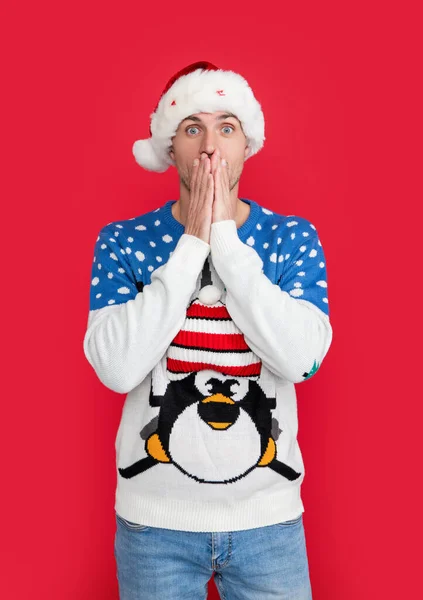 new year mood. shocked man isolated on red background wear new year sweater. man in new year santa hat.