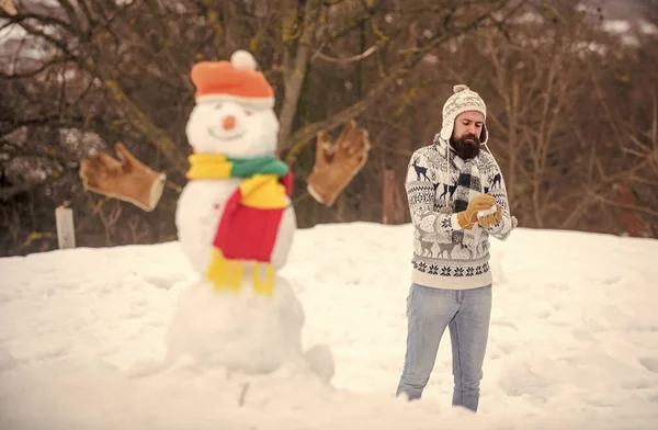 Snowman and cheerful bearded hipster knitted hat and warm gloves play with snow outdoors. Have fun winter day. Let it snow. Christmas holidays. Active lifestyle. Snow games. Leisure on fresh air.
