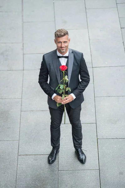 elegant man in tuxedo. man wearing bowtie suit outdoor. handsome tux man with red rose.