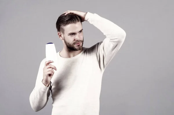 stock image Man touch hair with shampoo bottle in white tshirt on grey background. Hair care, salon, barbershop. Grooming, male beauty concept, copy space