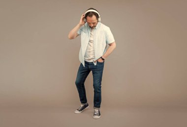 Son sınıf öğrencisi tam boy kulaklık takıyor ve müzik dinliyor. Gri arka plan, dinle..