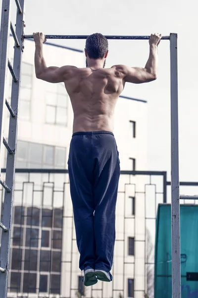 Man do chin ups outdoor. Sportsman pull up on stadium. Athlete with fit torso and strong hands on bar. Chin up bar exercises. Workout and training activity. Strength or power and sport, back view.