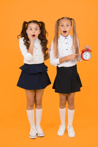 OMG. Got a surprise. Surprised schoolgirls checking time on yellow background. Shocked little children having mouth open with surprise being late. Back to school surprise. Surprise concept.