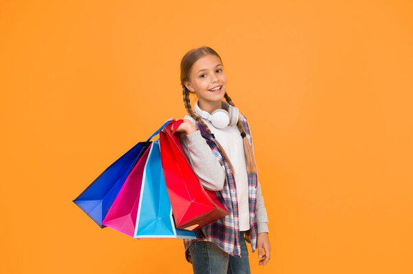 Dive into shopping. Happy child with paper bags. Little girl smile with shopping bags on yellow background. Holiday preparation and celebration. Shopping and sale on black friday. Addicted consumer.