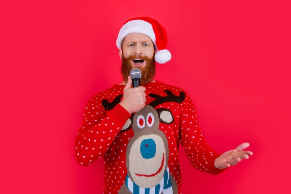 christmas music party. proud man at christmas music party with microphone. christmas santa man at music party isolated on red background.