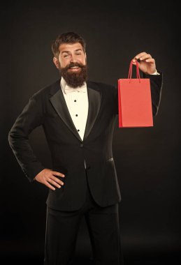 Siyah arka planda smokinli, papyon takan ve alışveriş çantalı gülümseyen adam. Alışveriş satışı. Boşluğu kopyala.