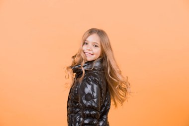 Moda, sonbahar bir tarz, trend. Turuncu arka plan üzerinde siyah palto kız. Mutlu çocukluk kavramı. Uzun sarı saçlı çocuk modeli gülümseme. Çocuk güzellik, göz, saç modeli, kopya alanı