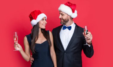 Mutlu Noel Baba çifti için Noel kutlaması. Noel Baba şapkalı çift kırmızıda izole edilmiş şampanya tutuyor. Noel Baba çifti için kurumsal Noel partisi. Stüdyodaki Noel Baba çifte mutlu Noeller..