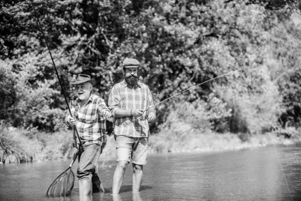 having fun. Fly Fishing Time. hobby. two happy fisherman with fishing rod and net. Camping on the shore of lake. hunting tourism. father and son fishing. Big game fishing. friendship.