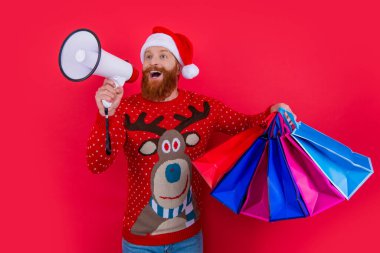 Sakallı adam elinde alışveriş torbalarıyla hoparlöre bağırıyor. Noel Baba indirim duyurusu yapıyor. Noel indirimi duyurusu. Dükkan duyurusu. Mutlu Noeller..