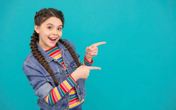 For your attention. Happy girl pointing index fingers at blue background. Little kid with pointing gesture. Pointing for advertising. Information for promoting. Promotion services, copy space.