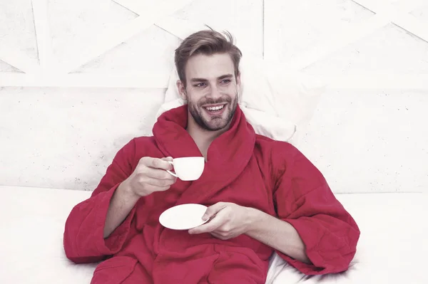 早餐喝咖啡 快乐的家伙在床上喝咖啡 穿着浴袍的胡子男子拿着酒杯 面带微笑 洗浴后享用茶或其他热饮 — 图库照片
