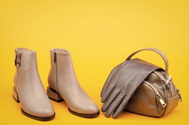 Ayakkabı dükkanı. kopyalama alanı. Kadın derisi şık ayakkabılar. Moda aksesuarı. Bir çift şık deri ayakkabı ve çanta. bej çizmeler ve eldivenler. Sarı arka planda bilek çizmeleri.