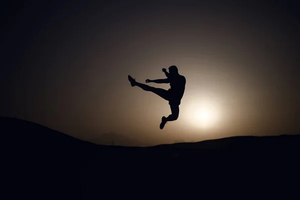 Athlete jump high with energy. Sportsman silhouette on sunset sky. Man training on natural landscape. Workout in summer dusk. Sport, wellness and bodycare concept.