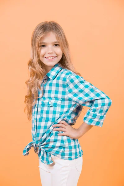 美しさ 長いブロンドの髪を持つ子モデル笑顔 ファッション スタイル トレンドを子供します 幸せな子供時代のコンセプトです オレンジの背景に青の格子縞のシャツの女の子 — ストック写真