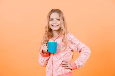 Sabah, Kahvaltı kavramı. Elinde kupa ile gülümseyerek mutlu bir çocuk. Turuncu zemin üzerine mavi Kupası ile bir gülücük. Yiyecek ve içecek. Çay ya da kahve ruh hali, punchy pastel, kopyalama alanı. soğuk, grip.