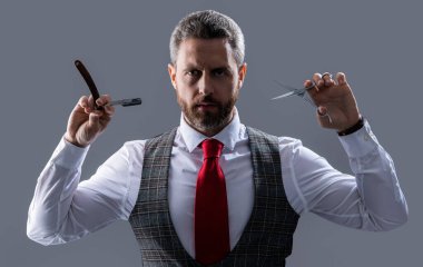 Adam kuaförle tıraş olur ve saç keser. Kuaför stüdyosunda berberlik yapan bir adam. Sakallı kuaför. Tıraşsız adam kuaför bıçak ve makas gri arka planda izole.