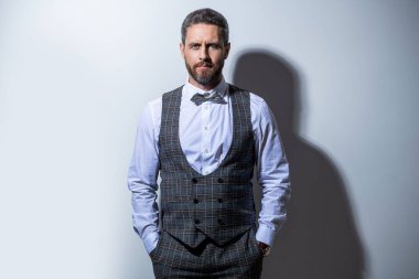 Smokin giyen adam resmi takım elbise giyer. Gri arka planda smokinli bir adam. Smokinli adam stüdyoda. Smokin giyen bir adamın fotoğrafı..