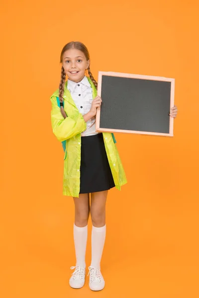 広告の配置 小さな子供は黄色の背景に関する情報のために空白の黒板を保持します 小さな女子高生はきちんとした情報ボードで笑顔 幸せな情報を共有する あなたの情報 コピースペース — ストック写真