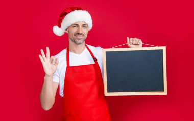 Yeni yıl şapkalı ve önlüklü mutlu olgun adam fotokopi alanı olan karatahtayı tutuyor. Tamam.