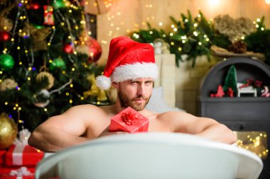 Keyfini çıkar. Kendimi şımartıyorum. Kış tatili Noel konsepti. Küvette yatan adam hediye kutusuyla rahatlar. Spa ve sağlık. Sıcak banyo. Sıcak banyo sağlık yararları. Noel Baba sıcak banyoda lüks içinde..