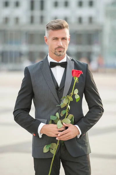 elegant man in tuxedo at romantic occasion. man with romantic present. charismatic romantic man with rose.
