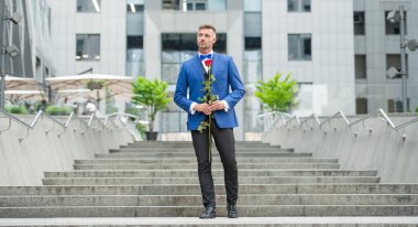 Smokinli zarif bir damat. Damat dışarıda smokin papyon takıyor. Kırmızı güllü lüks damat..