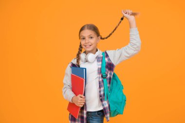 Uzun ve örgülü. Sevimli küçük okul çocuğu sarı arka planda uzun saç örgüsü tutuyor. Sevimli küçük kız uzun saç stili giyiyor. Okul için uzun saç stili.