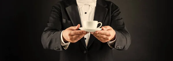 cropped man in tuxedo bow tie with coffee cup. waiter in formalwear hold coffee on black background.