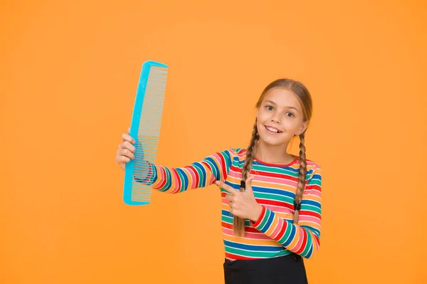 Comb for tangled hair. Hairdresser supplies. Large comb. Girl long hair hold enormous comb. Hairdresser salon. Combing hair. Cheerful happy smiling little kid with giant comb. Professional equipment.