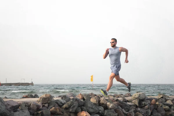 Pain is nothing compared to what it feels like to quit. Running man on beach. Runner training outdoors. Fit male sport fitness exercising in summer. Running sport and hobby. Man fitness coach.